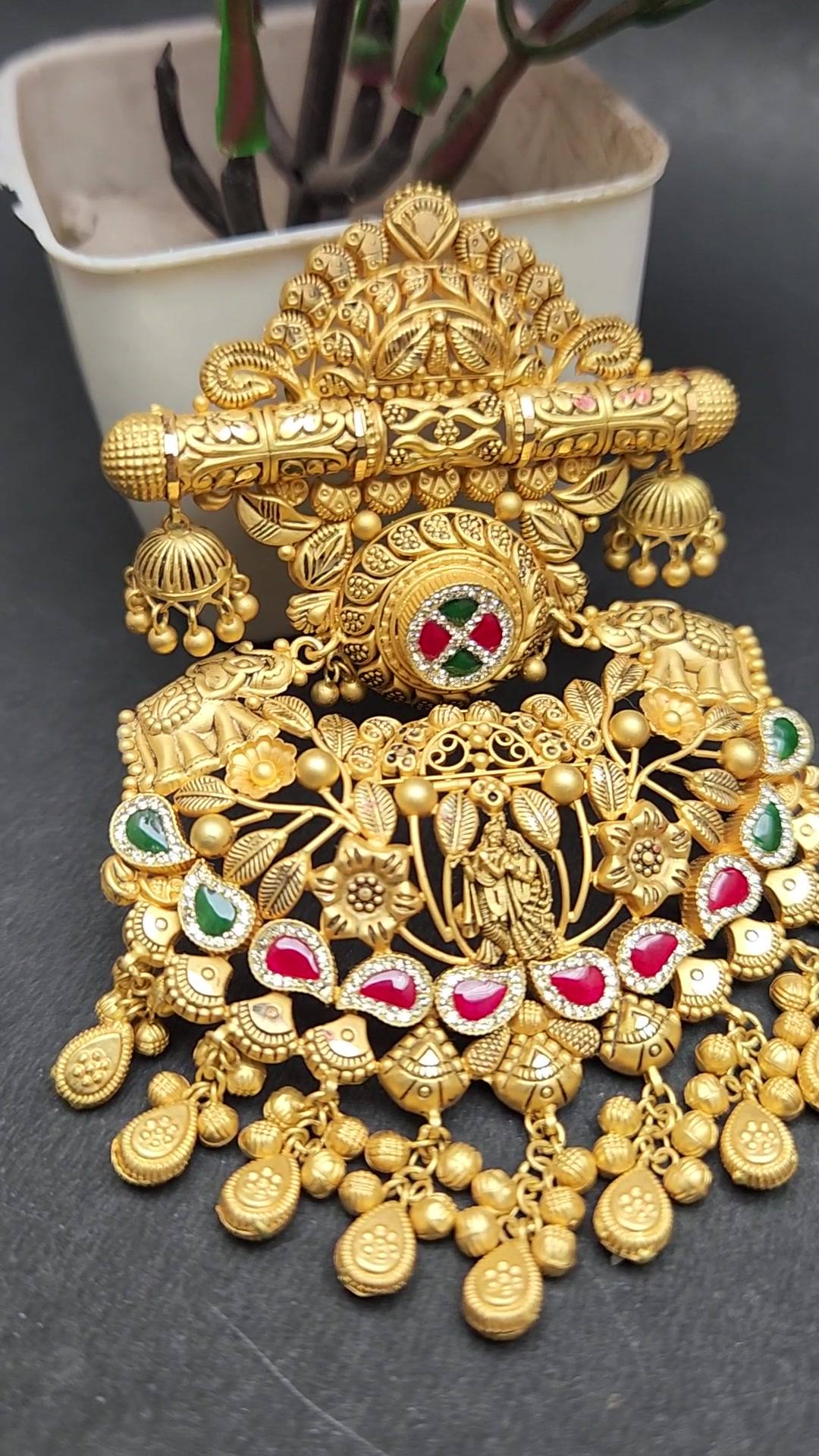 A gold pendant set with ruby-red and emerald-green stones, turning slowly