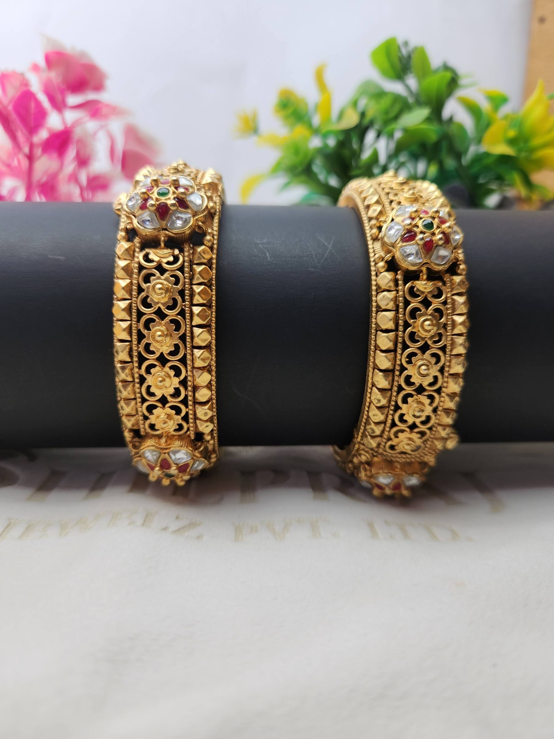 Pair of matte gold kadas with floral jaali, pyramid studs and white stone flowers with red and green centres