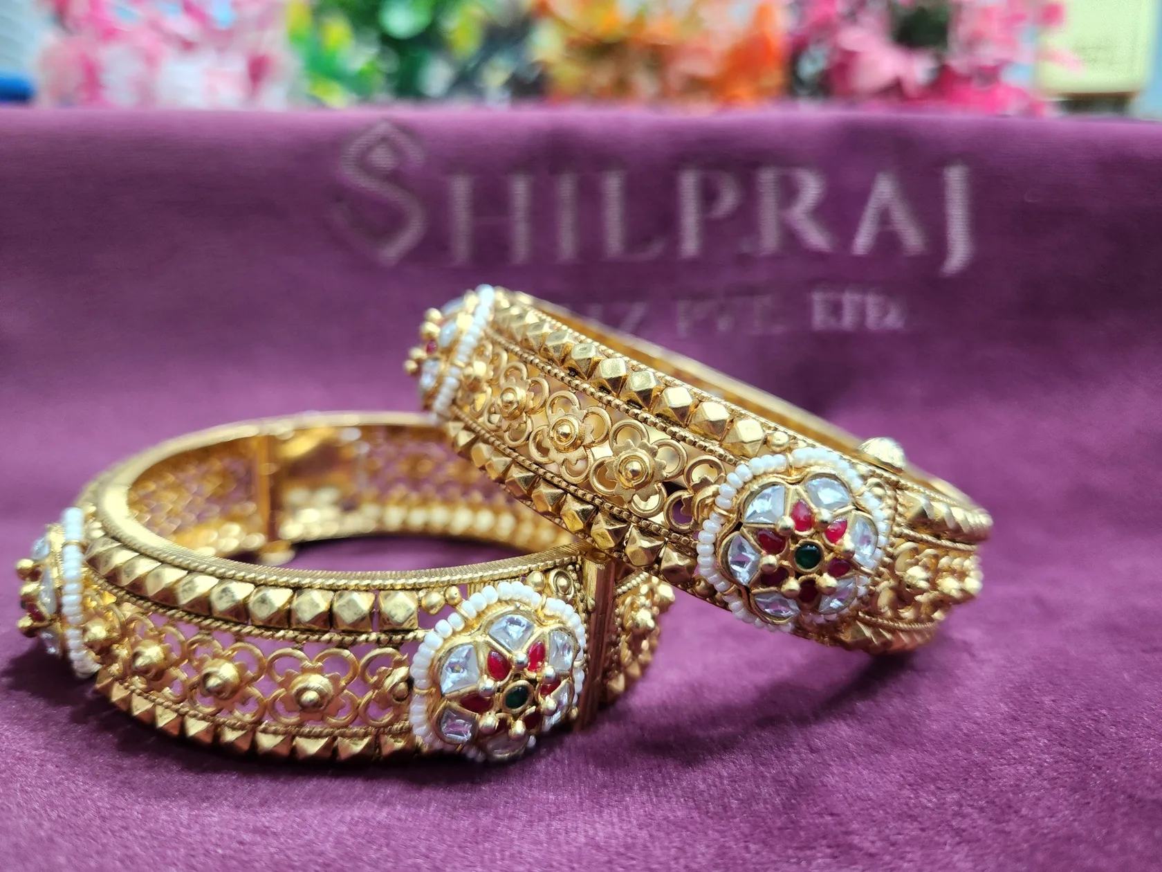 Two matte gold kadas with filigree, pyramid studs and pearl-ringed flowers of white, red and green stones