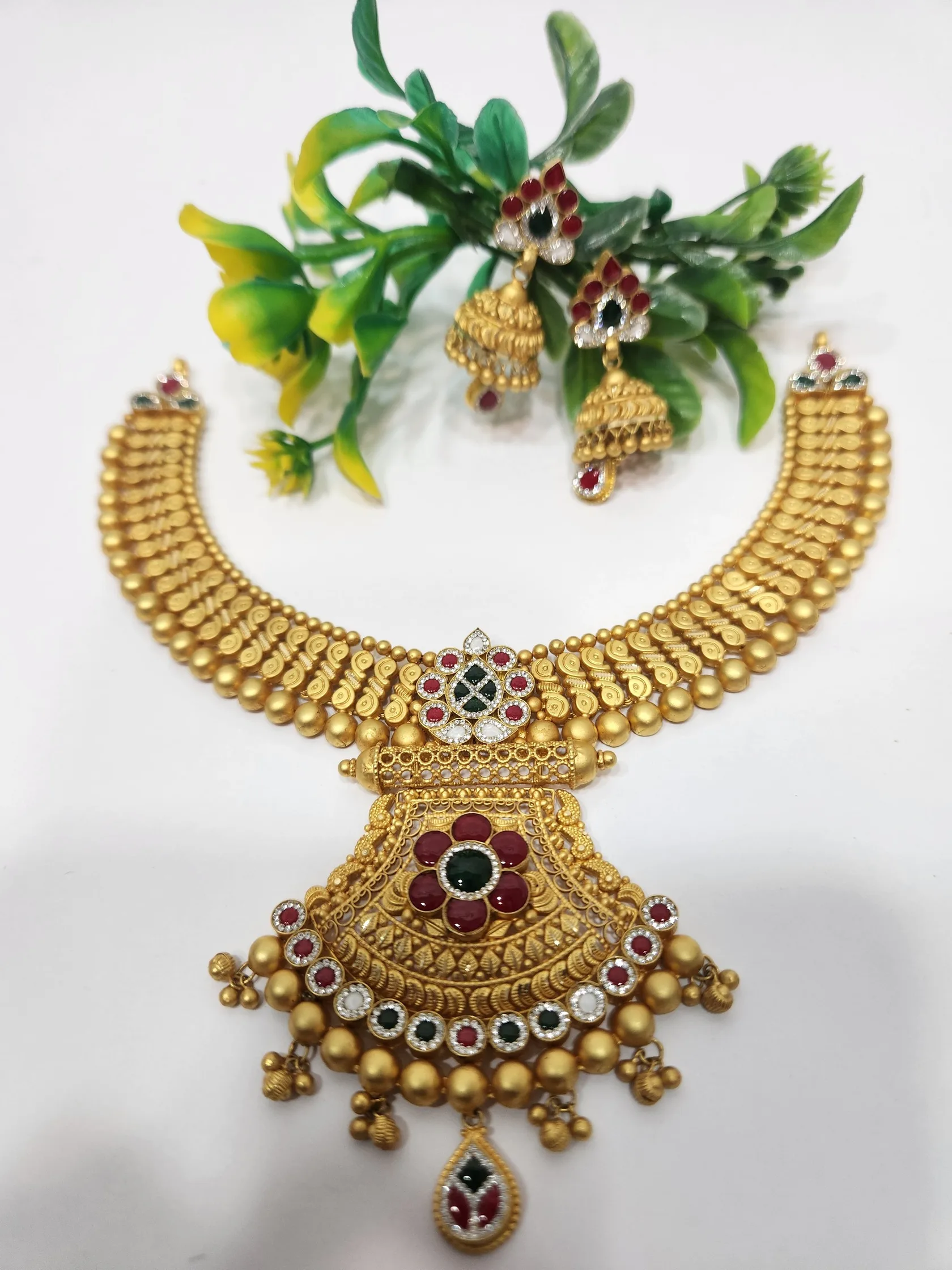 Matte gold collar necklace with fan-shaped pendant, red and green stones, bell fringe and matching jhumkas