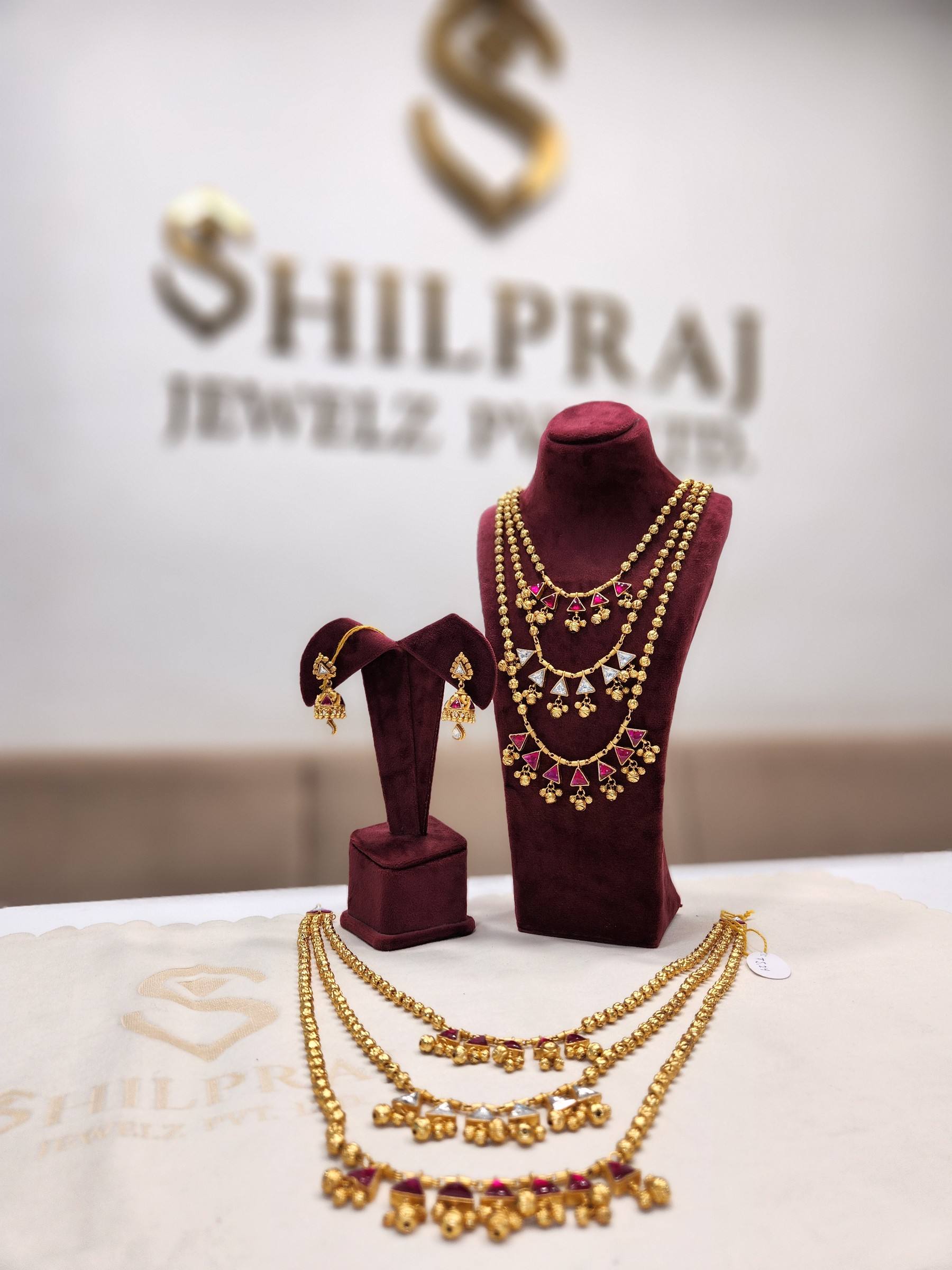 A layered gold necklace on display before the Shilpraj Jewelz name