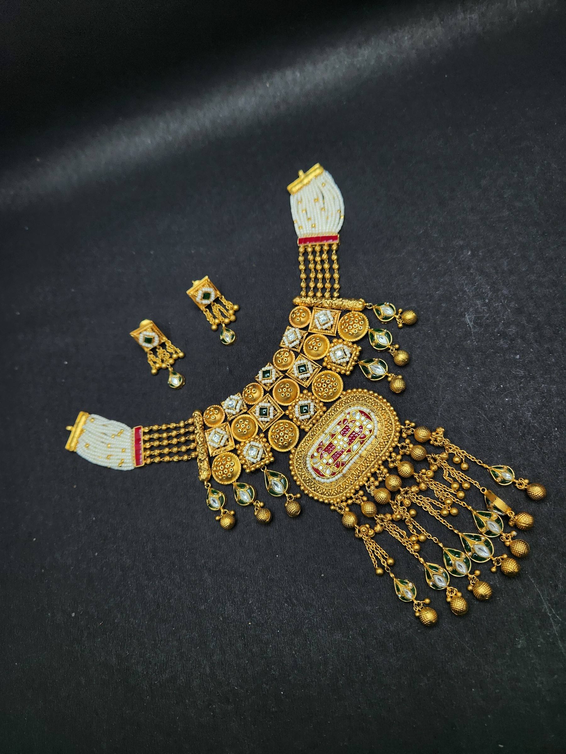Rajasthani-style gold necklace with a jaali of stone-set squares, oval red and white pendant, chain tassels and earrings