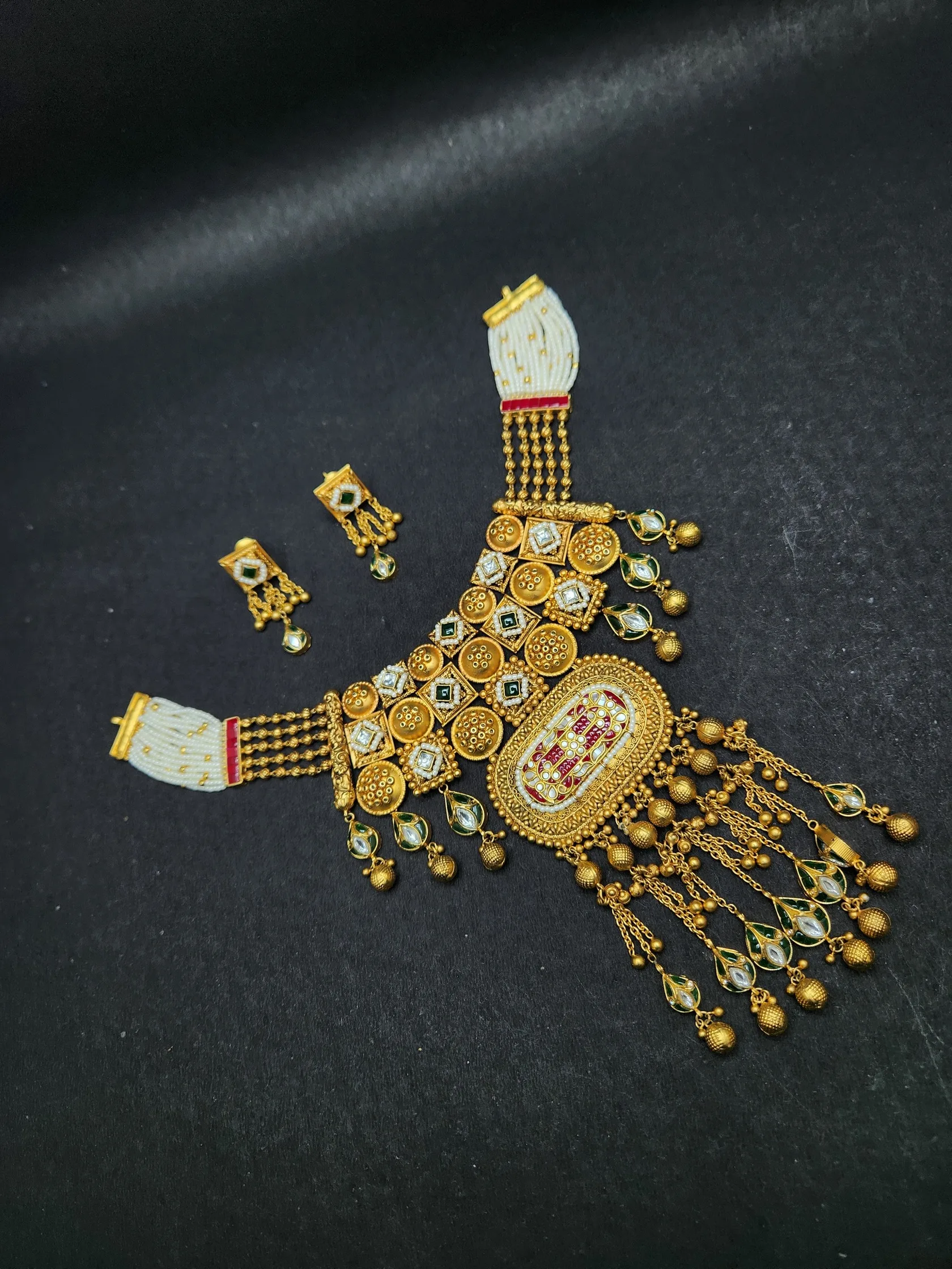 Rajasthani-style gold necklace with a jaali of stone-set squares, oval red and white pendant, chain tassels and earrings