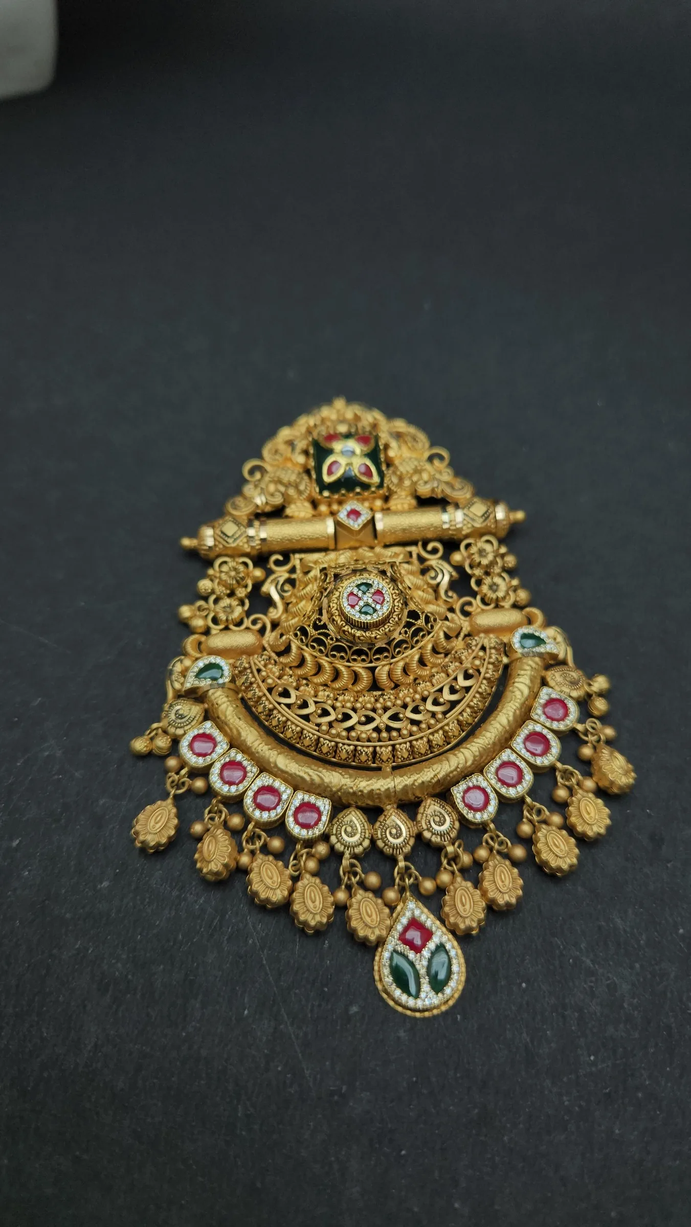 Gold pendant with filigree crescent, ribbed bar, red stones framed in white, leaf fringe and a drop-shaped stone
