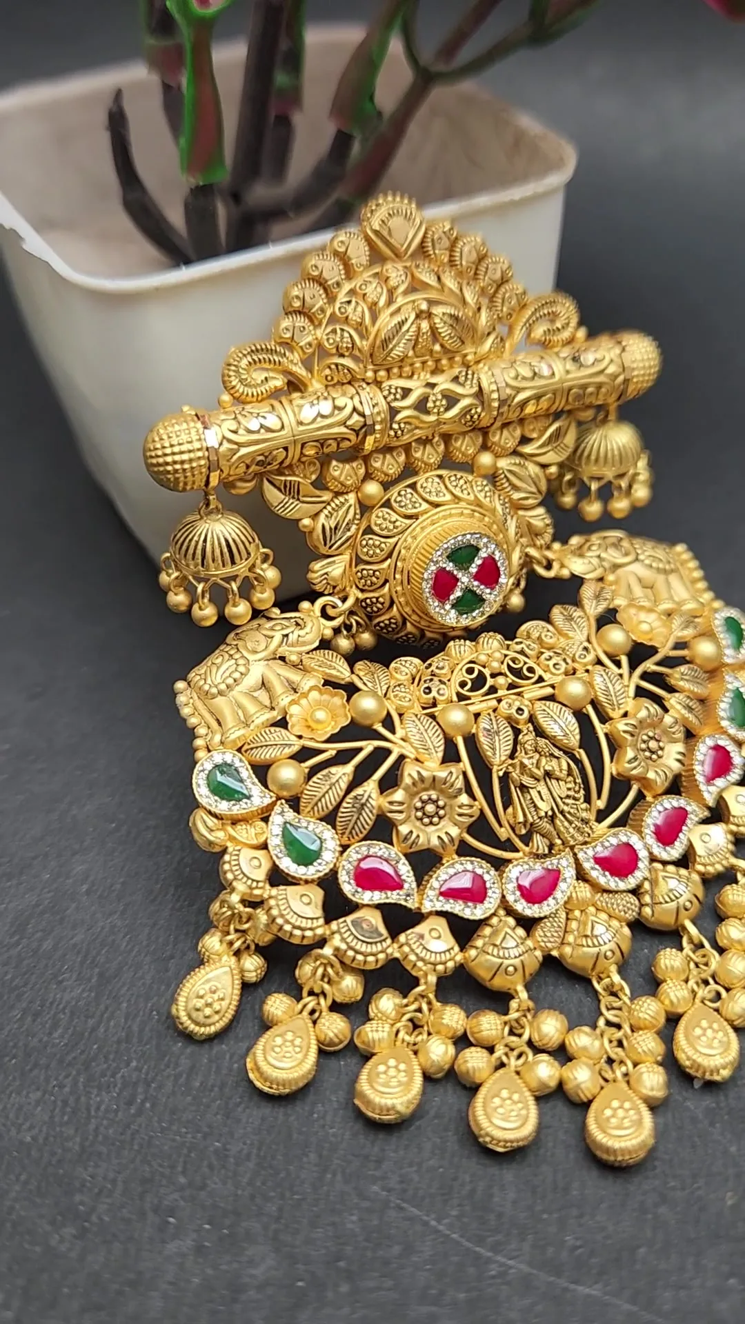 Matte gold pendant with filigree crown, ribbed bar with small jhumkas, red and green stone medallion and bead fringe