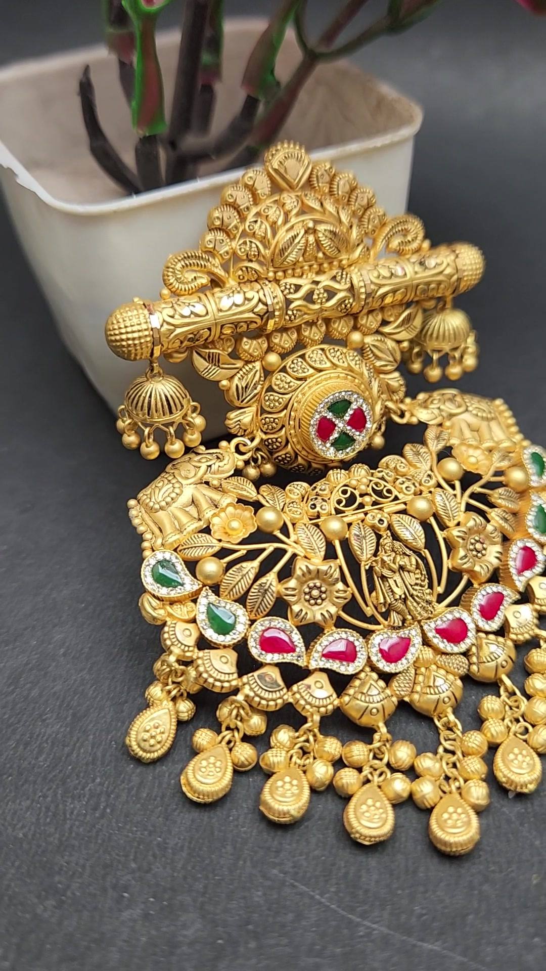 Matte gold pendant with filigree crown, ribbed bar with small jhumkas, red and green stone medallion and bead fringe